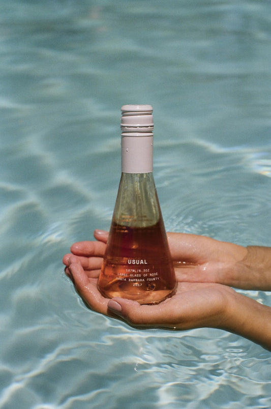 Person holds Usual Wines Rose over sparkling pool