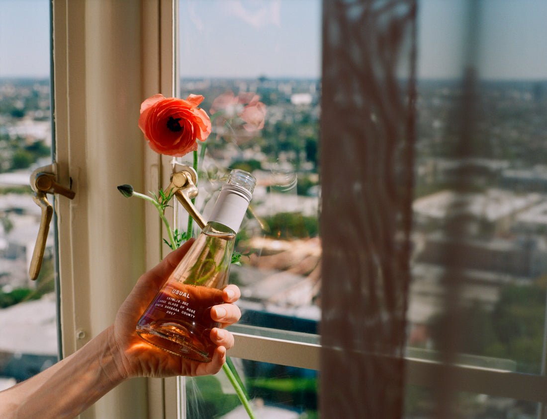 Holding rose wine and a flower next to a window