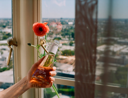 Holding rose wine and a flower next to a window