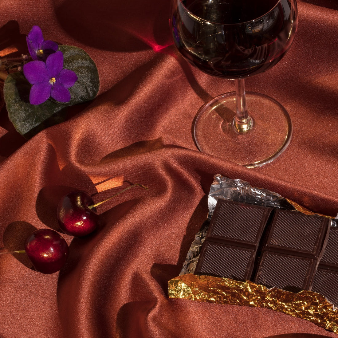 malbec wine: wine glass, cherries and chocolate on top of rusty colored table cloth