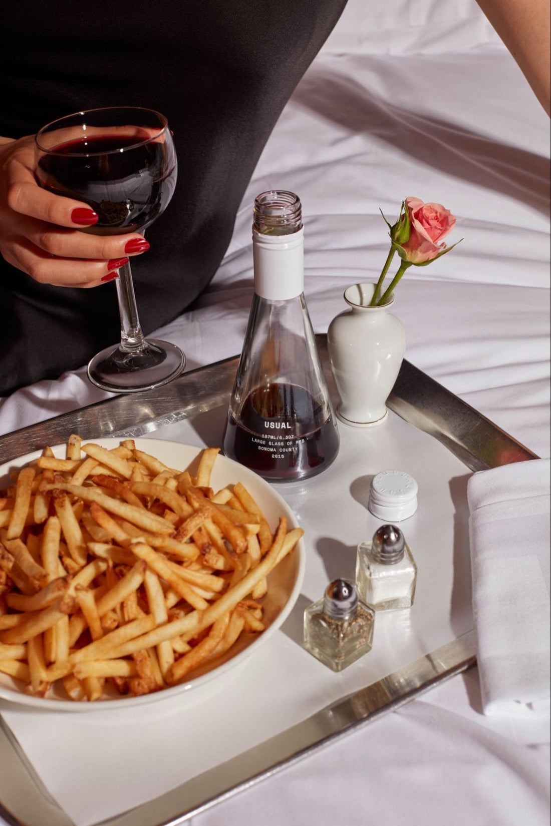 sweet red wine: person holding a glass of red wine from Usual Wines with a plate fries on a silver platter