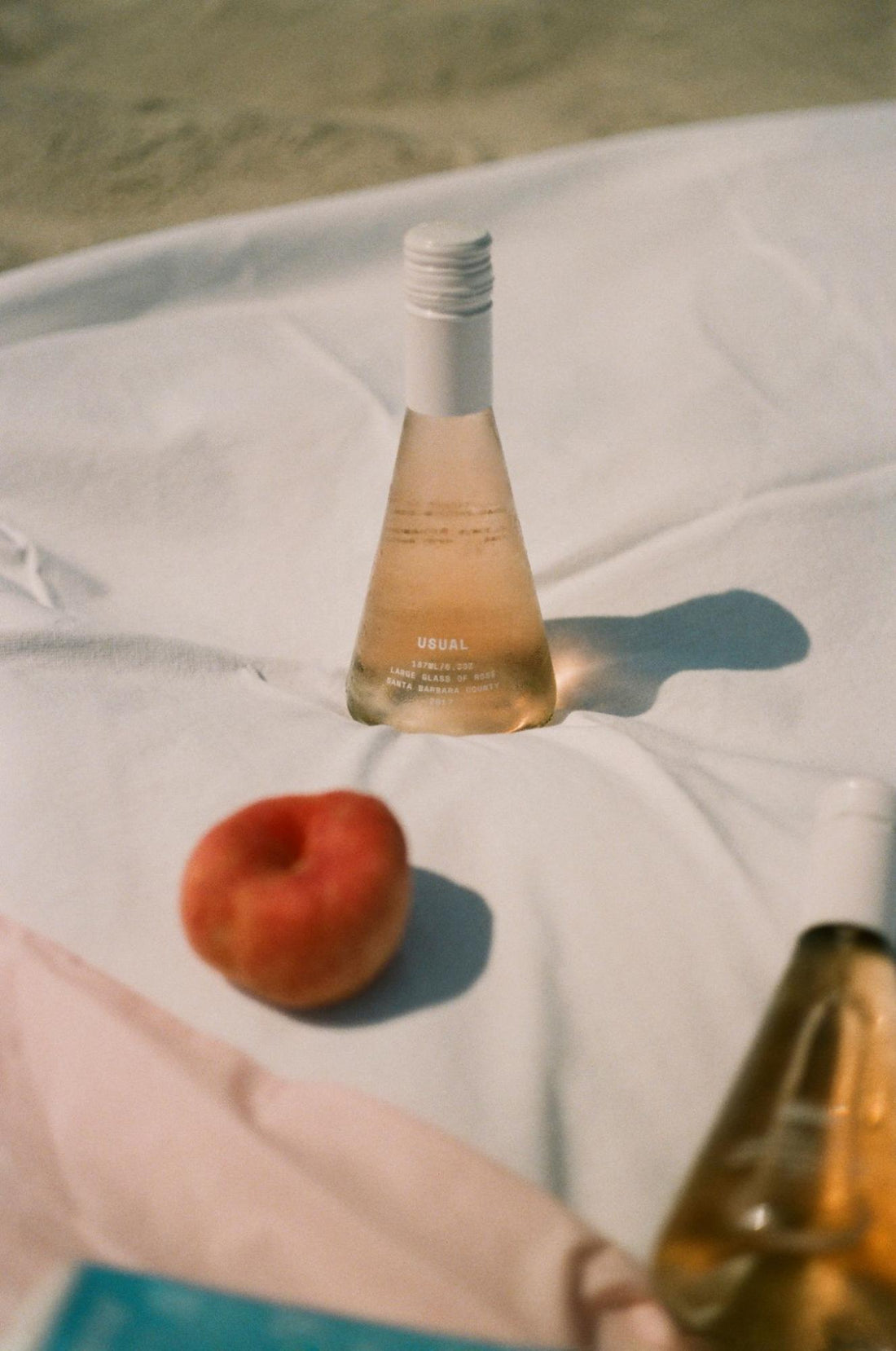 wine cocktails: bottles of Rosé with a peach on a cloth outdoors