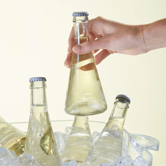 A woman's hand grabbing a bottle of white wine out of a large iced bucket with more wine inside it.